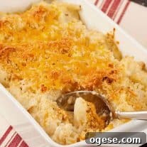 Golden brown roasted cauliflower gratin topped with melted cheddar cheese and crispy breadcrumbs in a white baking dish with serving spoon.