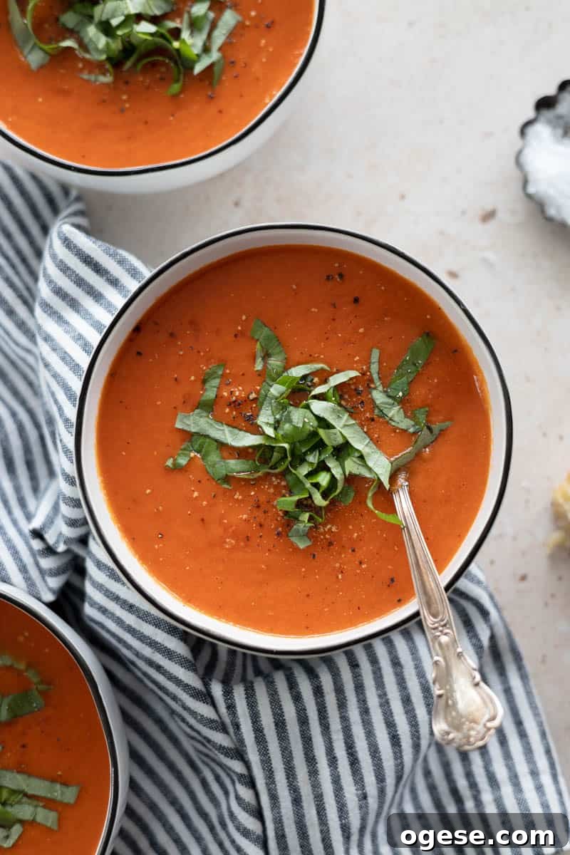 Roasted Red Pepper and Tomato Soup Recipe for Cozy Weeknights 2 A bowl of Roasted Red Pepper and Tomato Soup topped with fresh basil, served with a spoon and blue and white striped linen.
