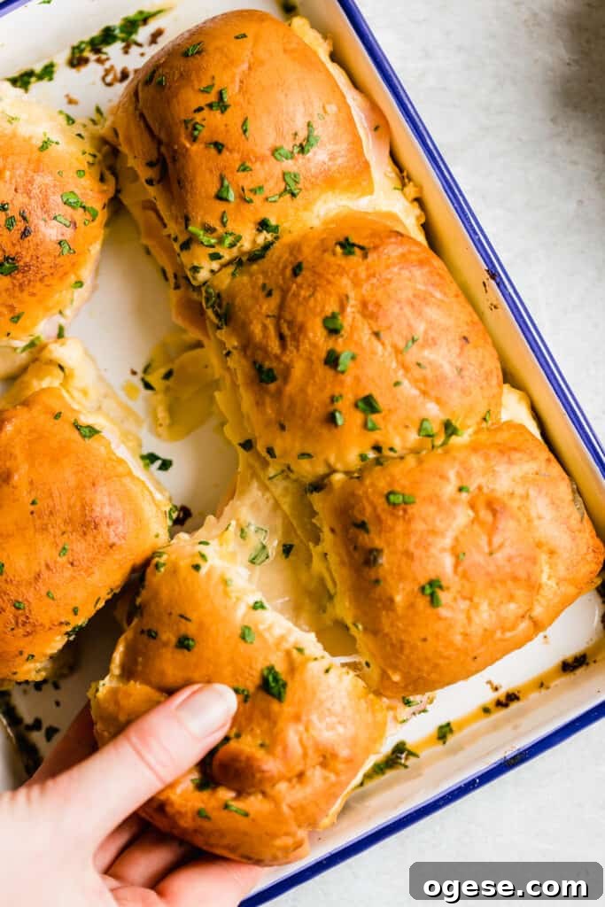 Savory Ham and Swiss Sliders with Honey-Dijon Glaze 3 A Hand Grabbing a Ham and Cheese Slider From a Blue-Rimmed Pan