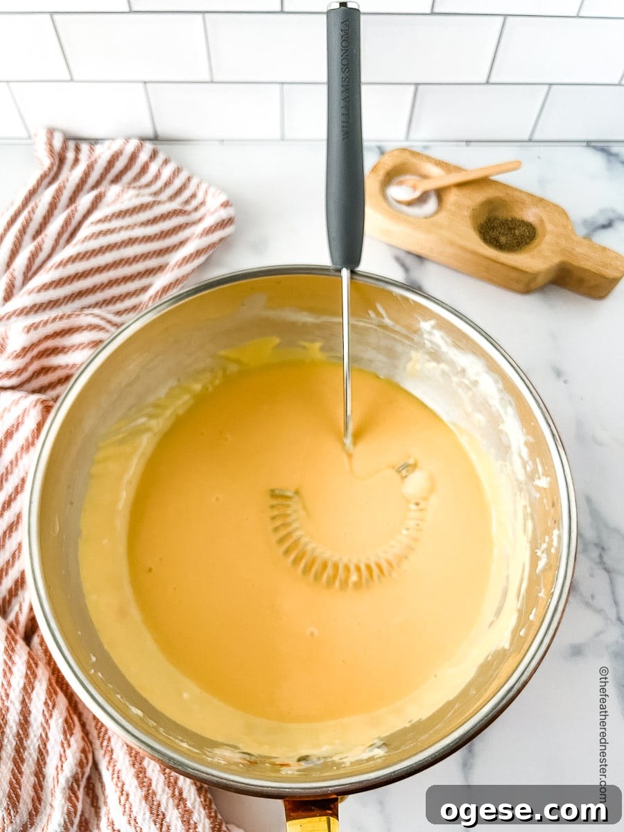 Creamy yellow sauce in a large bowl with a whisk.