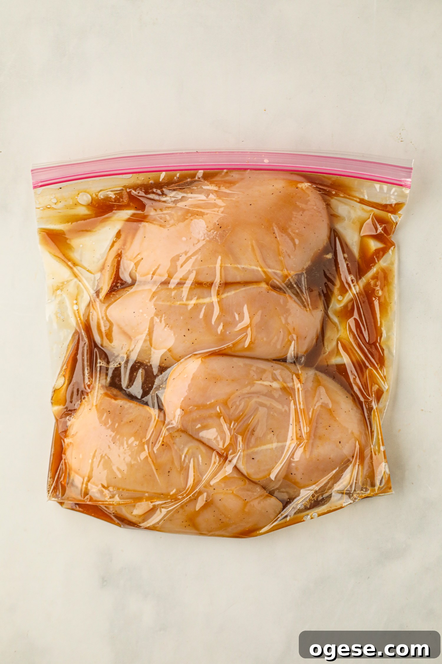 Grilled Pineapple Chicken with Tangy Glaze and Charred Pineapple 4 The image shows raw chicken breasts marinating in a resealable plastic bag with a dark-colored liquid marinade.