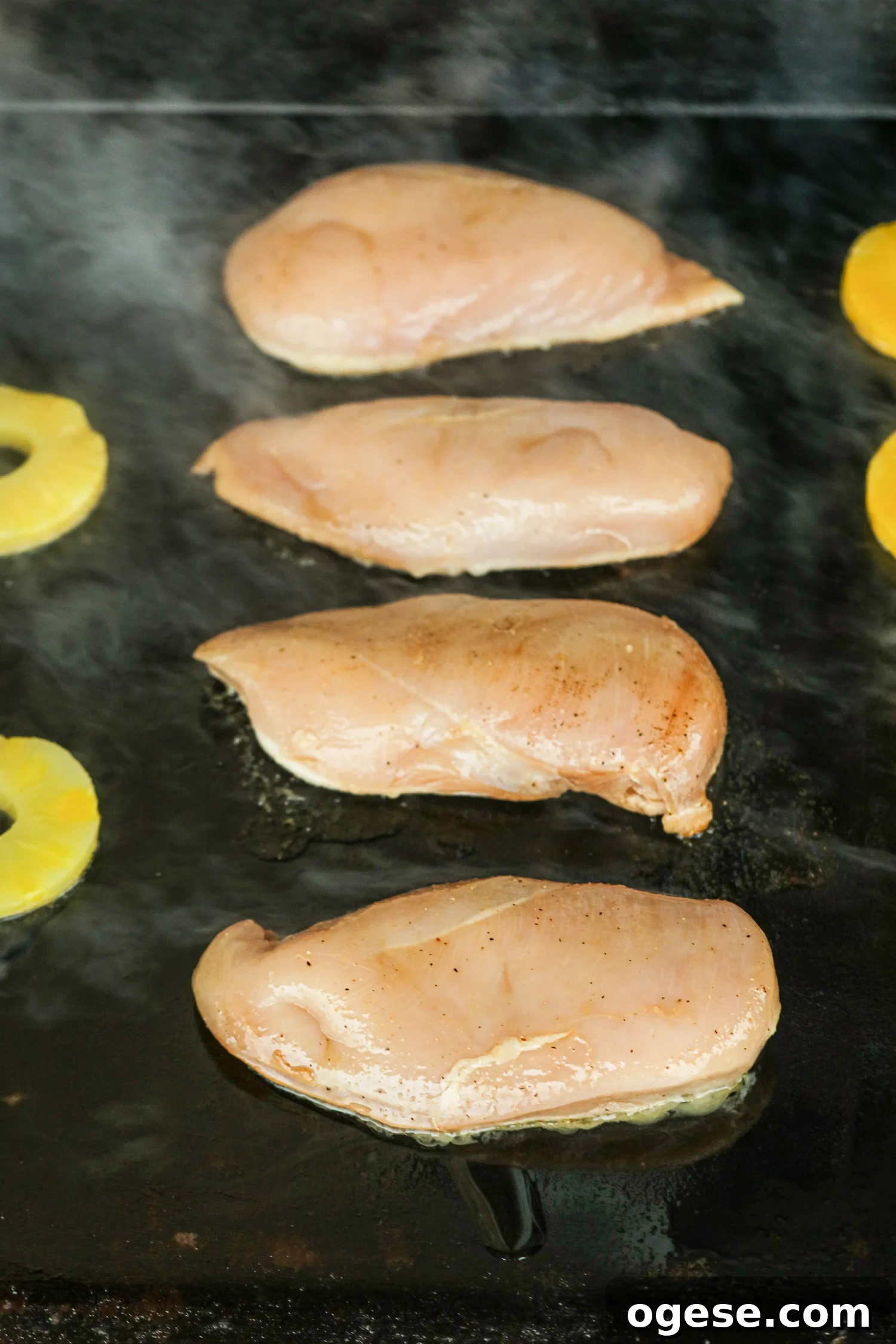 Grilled Pineapple Chicken with Tangy Glaze and Charred Pineapple 5 The image shows four chicken breasts and pineapple slices on a hot griddle beginning to sear.