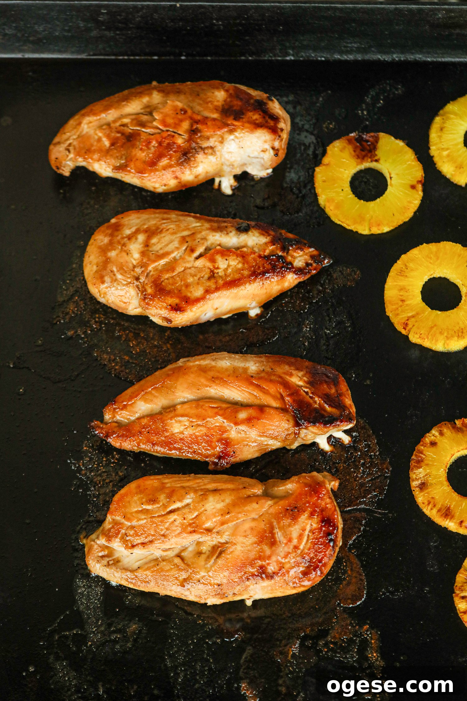 Grilled Pineapple Chicken with Tangy Glaze and Charred Pineapple 7 Grilled chicken breasts and pineapple slices cooking on a black griddle with visible sear marks.
