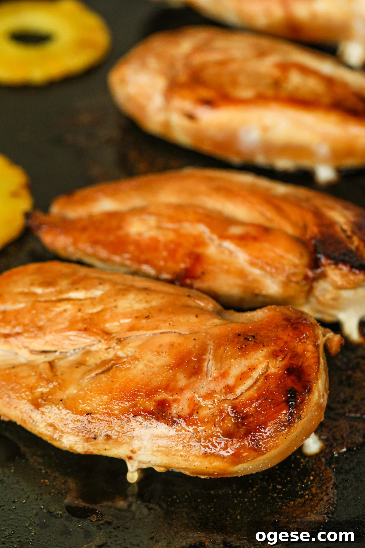 Grilled Pineapple Chicken with Tangy Glaze and Charred Pineapple 8 Close-up of grilled chicken breasts with grill marks and juices, with grilled pineapple in background.