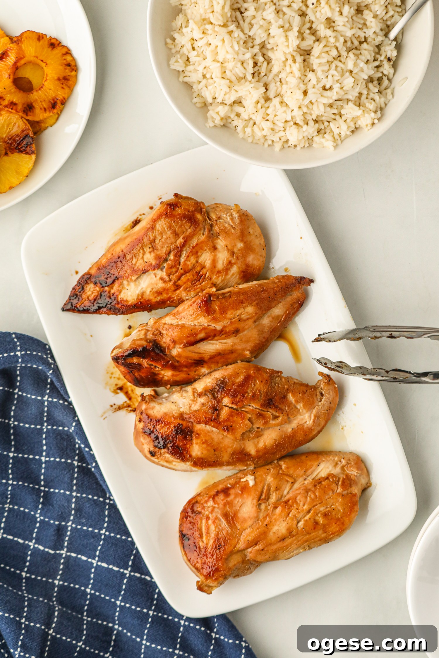 Grilled Pineapple Chicken with Tangy Glaze and Charred Pineapple 9 A white plate with grilled chicken breasts and a bowl of rice, with grilled pineapple on the side.