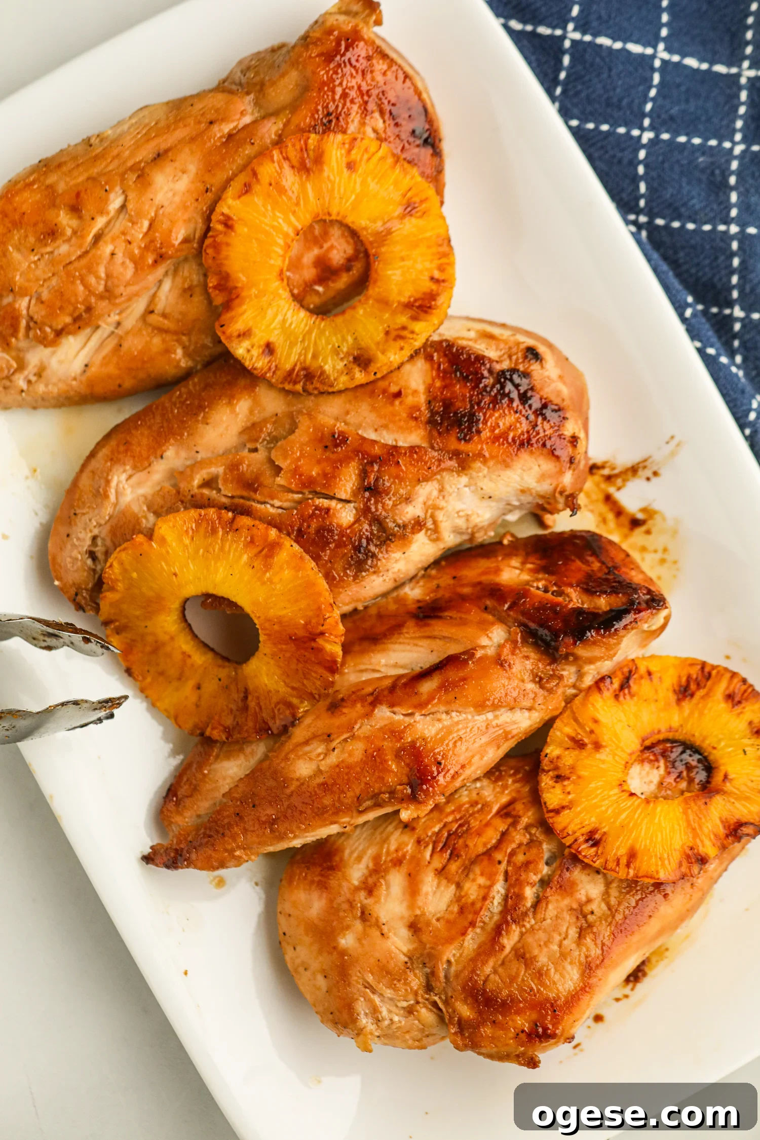 Grilled Pineapple Chicken with Tangy Glaze and Charred Pineapple 10 Grilled chicken breasts each topped with a caramelized pineapple slice on a white plate.