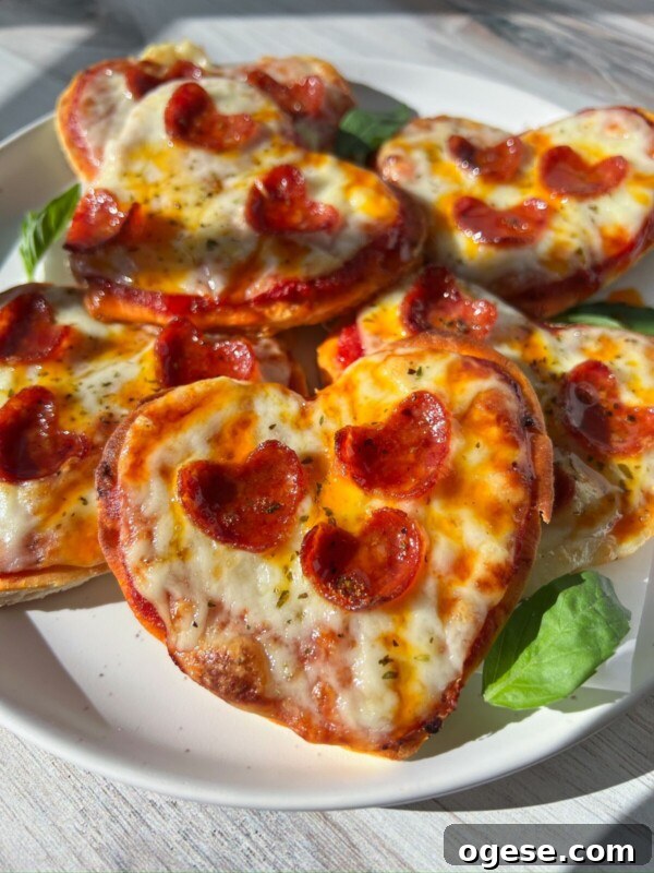 Romantic Valentine's Day Appetizers to Impress Your Date 3 A plate of Heart Shaped Pizza minis, topped with melted cheese and small pepperoni slices, garnished with fresh basil leaves, sits in bright natural sunlight.