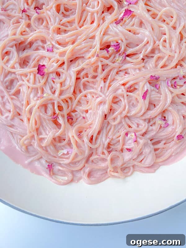 Romantic Valentine's Day Appetizers to Impress Your Date 5 Close-up of Pink Pasta coated in a creamy, pastel pink sauce, garnished with small pink flower petals, served in a white bowl.