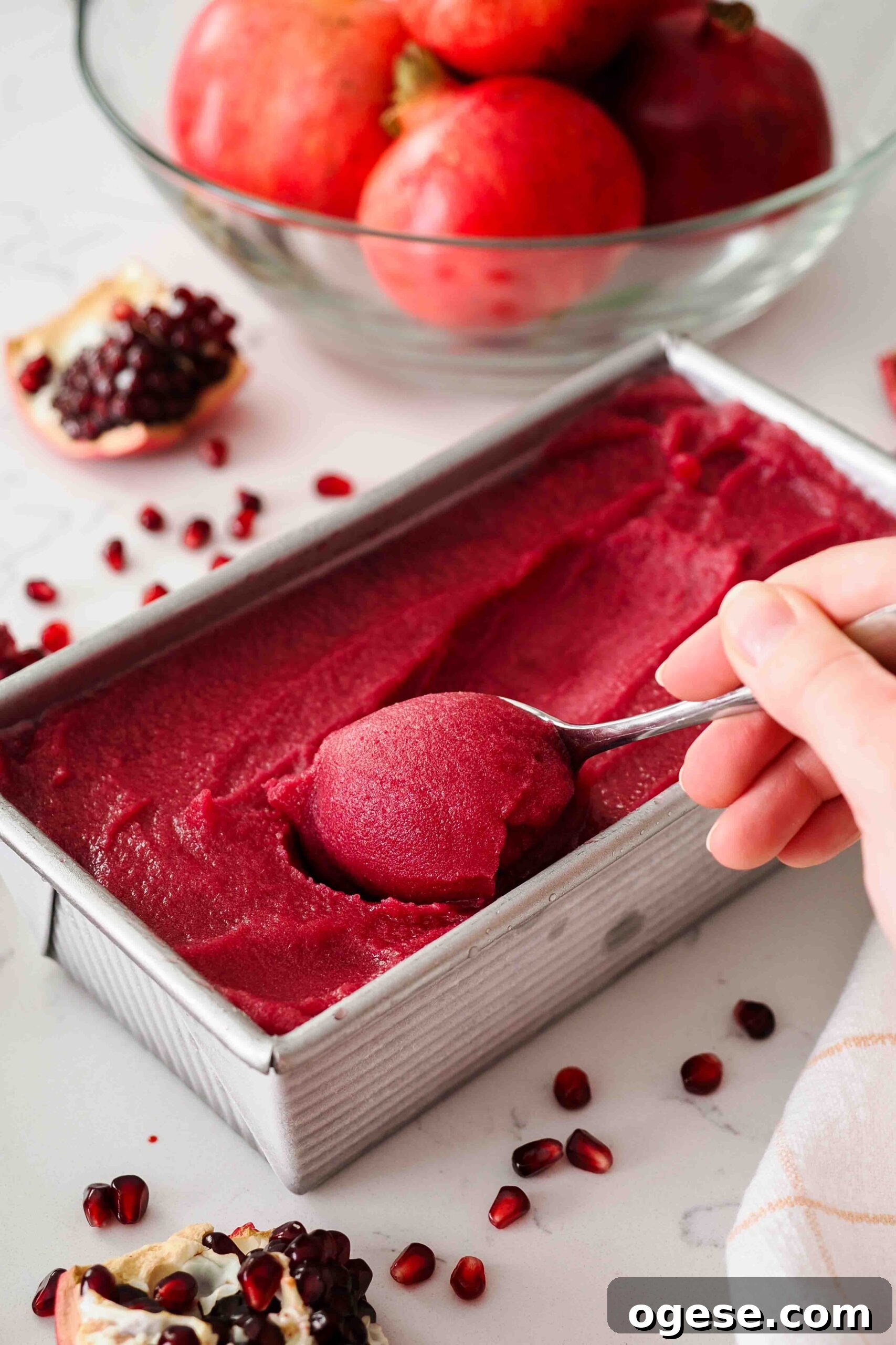 A teaspoon scoops up soft pomegranate sorbet from a loaf tin.