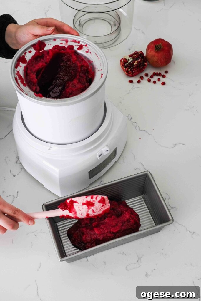A spatula scoops pomegranate sorbet out of an ice cream maker and into a chilled loaf tin.