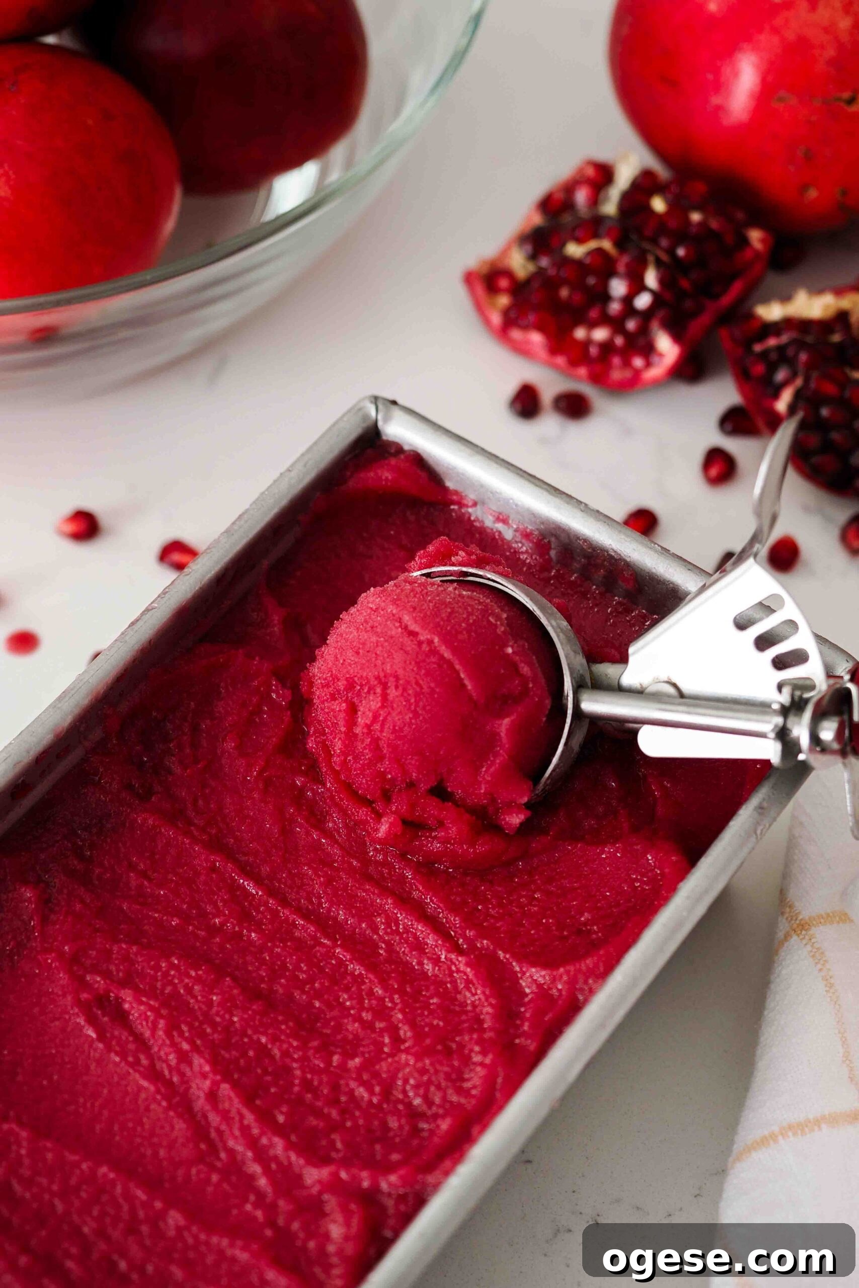 An ice cream scoop filled with pomegranate sorbet over a loaf tin of sorbet.
