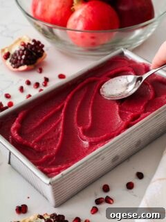 A spoon creates swirls in pomegranate sorbet in a loaf tin.