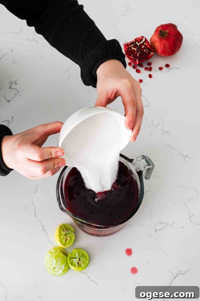 Two hands pour sugar into a pomegranate juice-filled measuring cup.