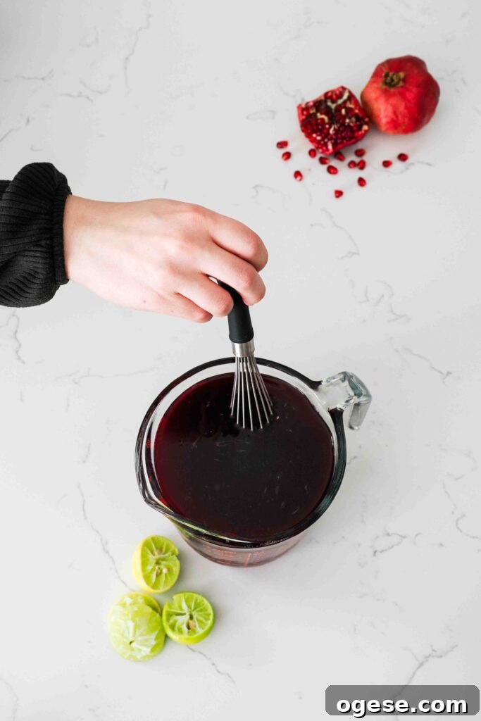 A whisk stirs pomegranate sorbet mix in a measuring cup.