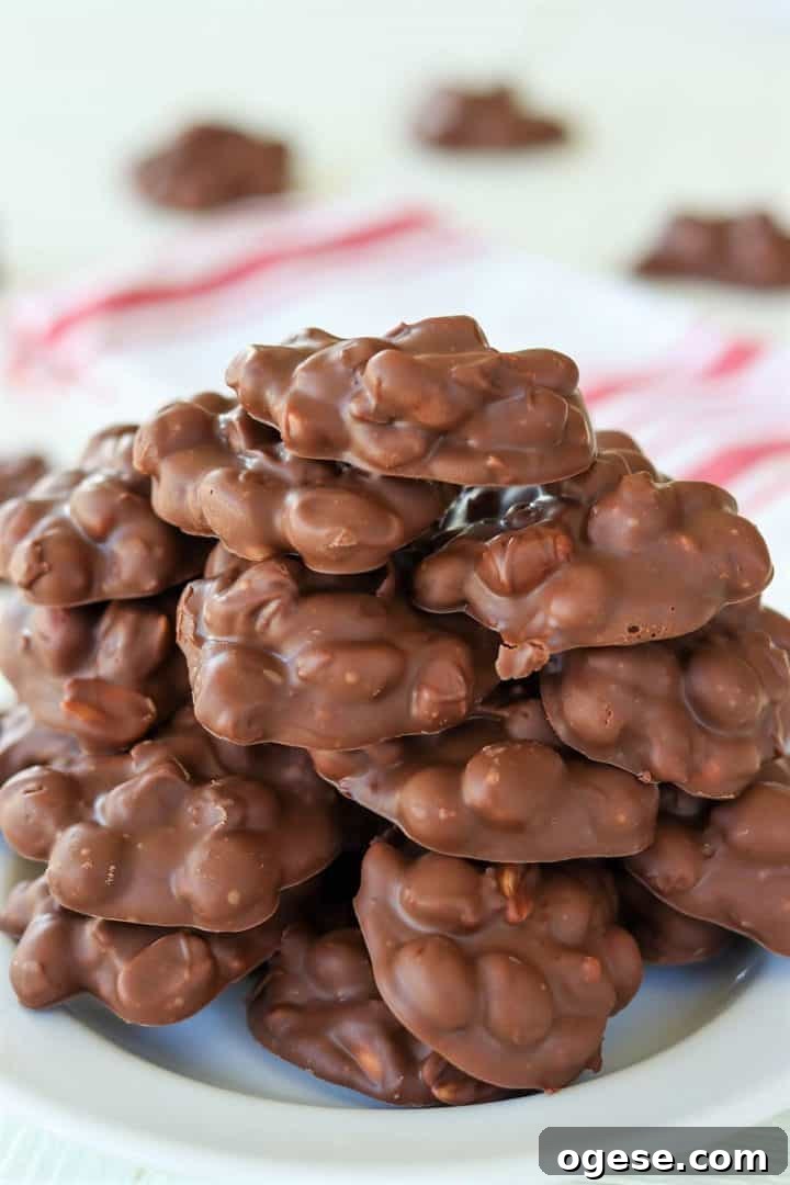 4-Ingredient Crockpot Peanut Clusters Recipe 2 Portrait image of peanut clusters stacked on a white plate ready for eating. A red and white napkin is in the background.