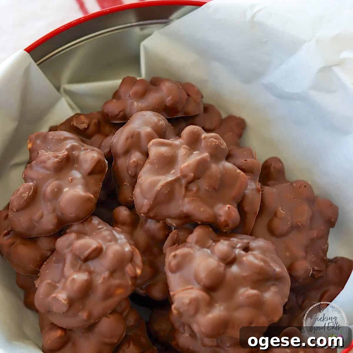 4-Ingredient Crockpot Peanut Clusters Recipe 8 Crockpot chocolate peanut clusters in a round red metal tin with parchment paper.