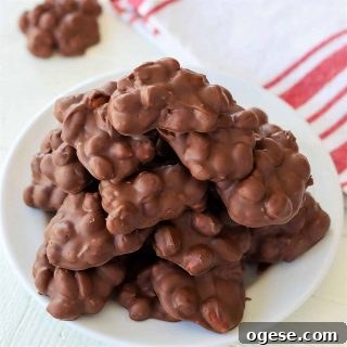 4-Ingredient Crockpot Peanut Clusters Recipe 9 Feature image closeup of peanut clusters piled high on a white plate with a red and white striped napkin in the background.