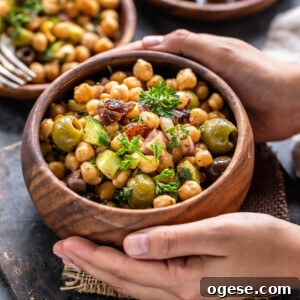 pair of hand holding a bowl of chickpea salad served in a wooden bowl