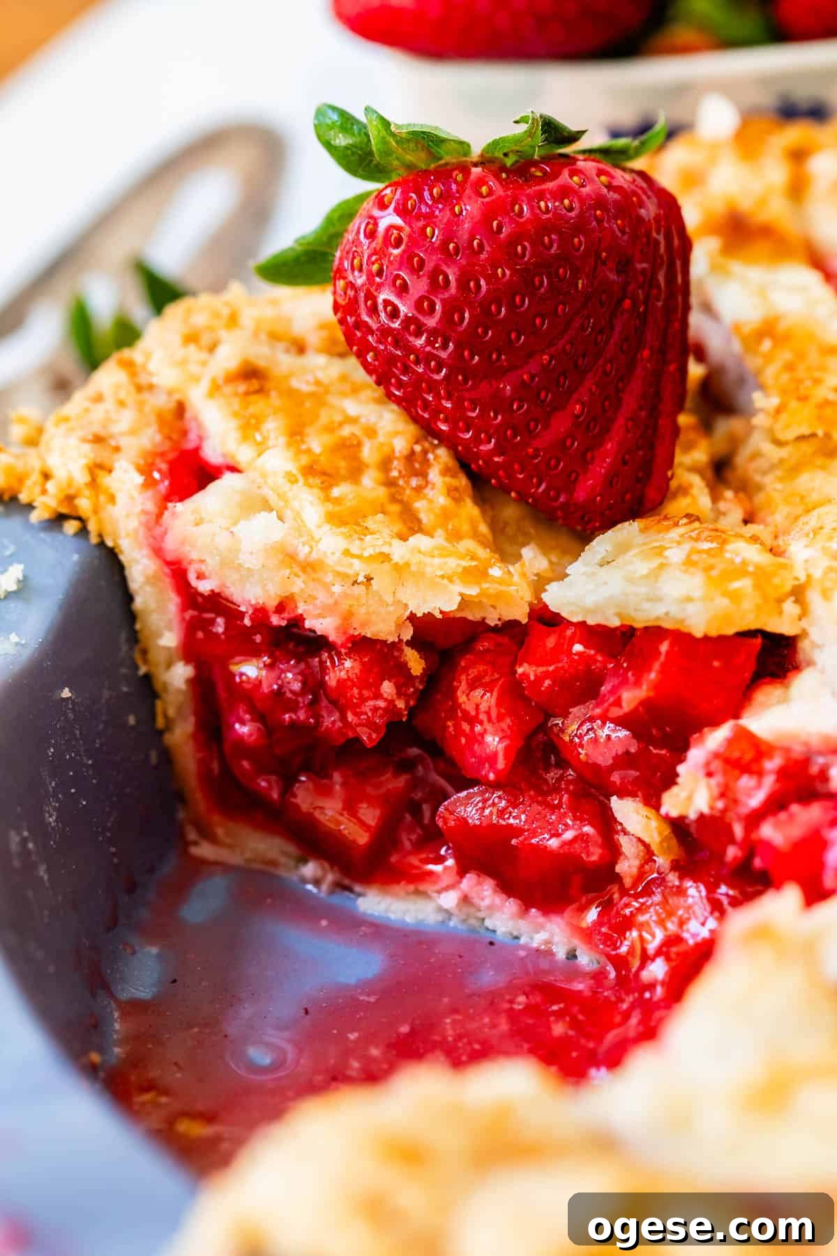 side view with all the strawberry rhubarb filling of a piece of pie in a pie pan with strawberry garnish.