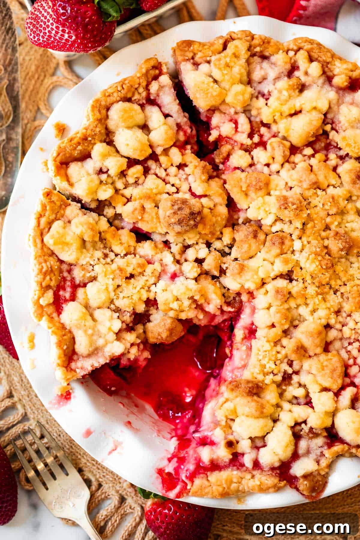 whole crumble topped rhubarb strawberry pie with slices cut and one removed from pan.