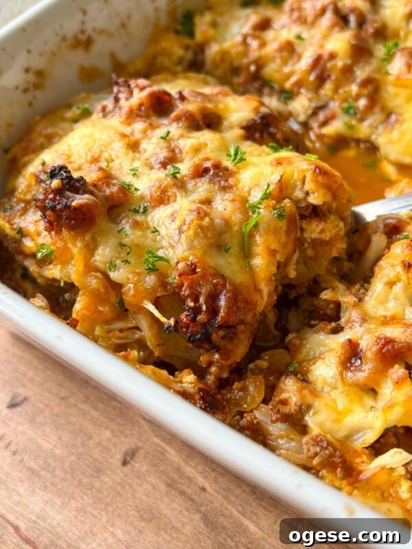 Close-up of a baked Cabbage Lasagna in a white dish, featuring a golden, melted cheese topping with browned edges and sprinkled with fresh chopped herbs. A serving spoon is lifting a portion from the dish.