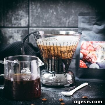 Filled clever dripper placed on dark ground, next to coffee filled glass carafe.