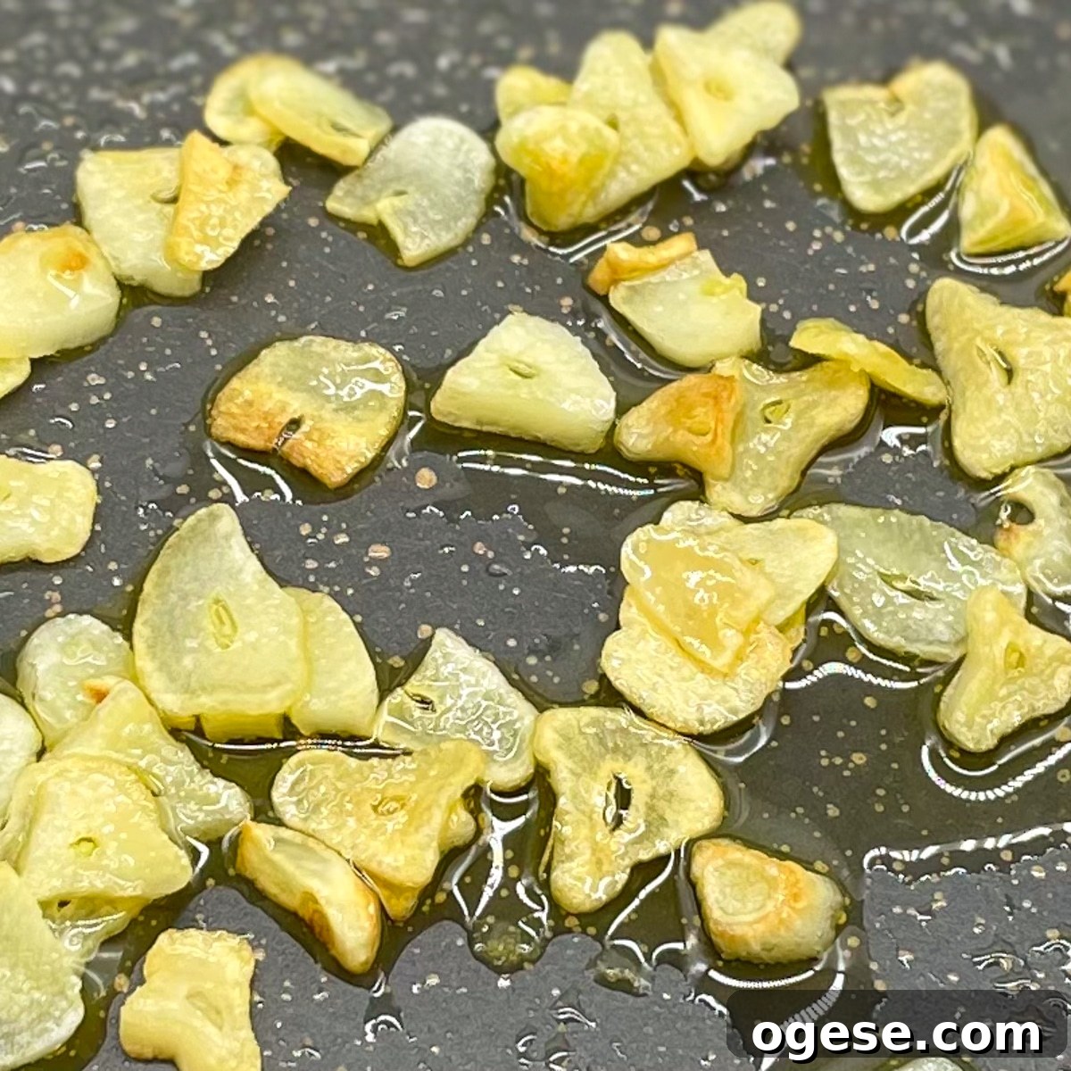 Sliced garlic cooking in olive oil in a gray frying pan