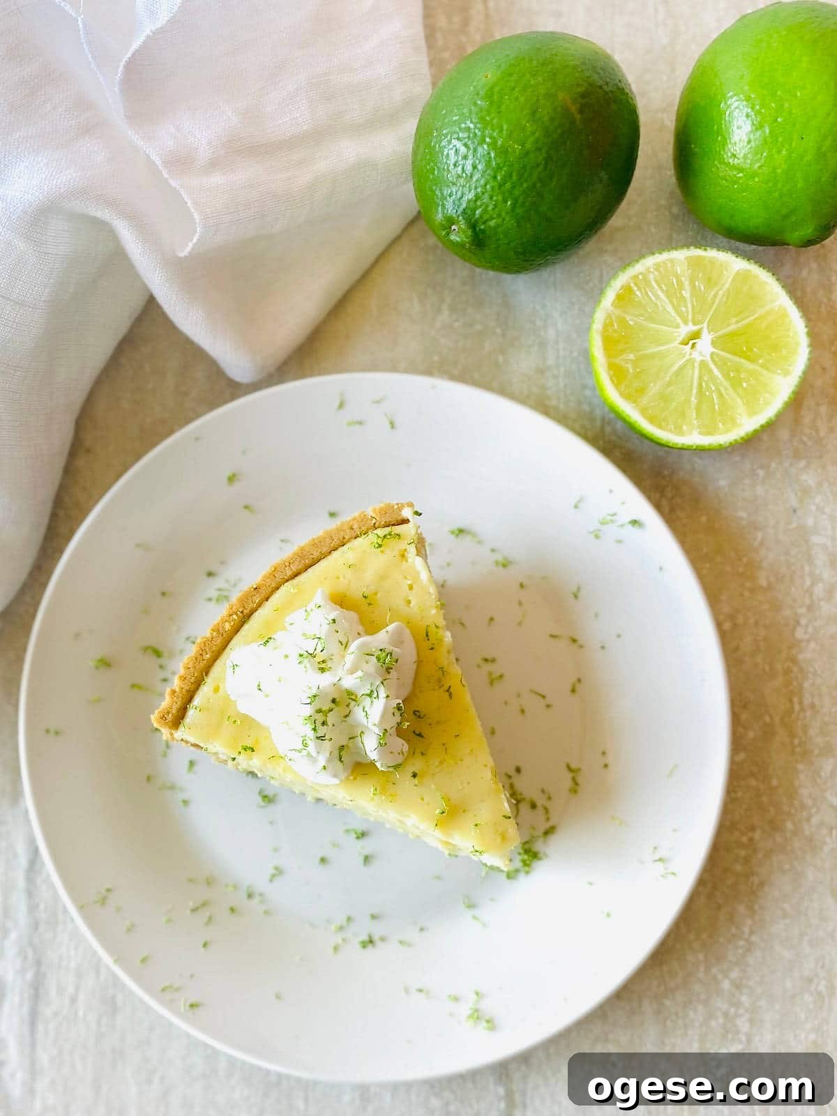 gluten free key lime pie on a plate next to limes topped with whipped cream and lime zest
