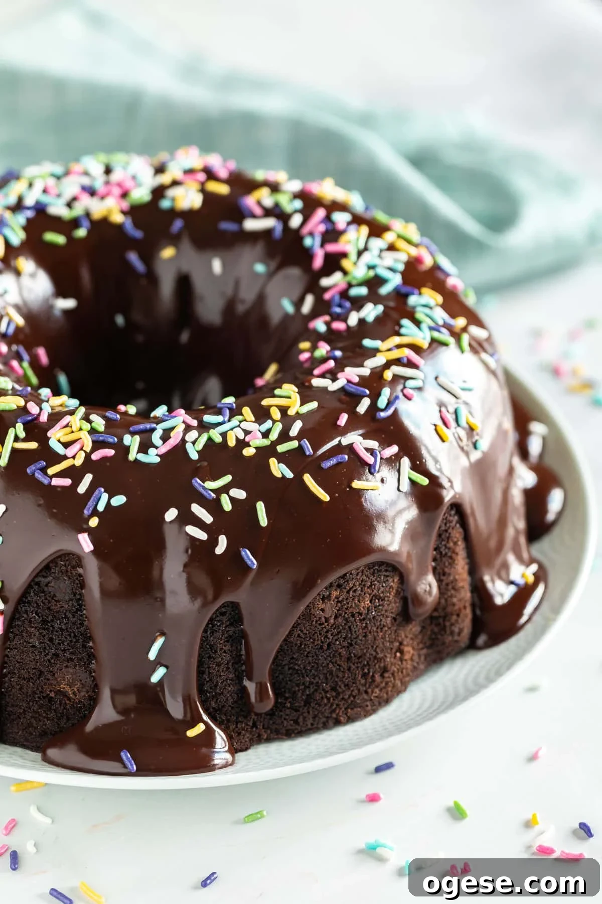 Ultimate Chocolate Overload Cake Recipe for True Chocoholics 2 Chocolate bundt cake with chocolate ganache dripping down the sides and sprinkles on top with a teal napkin behind it.