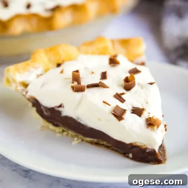 A close up image of a slice of chocolate pudding pie on a white plate with the rest of the pie behind it.