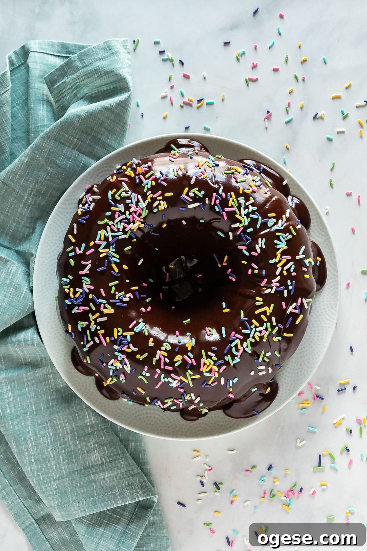 Ultimate Chocolate Overload Cake Recipe for True Chocoholics 3 A overhead image of a bundt cake with ganache and sprinkles on top with a teal napkin and other sprinkles on the side.