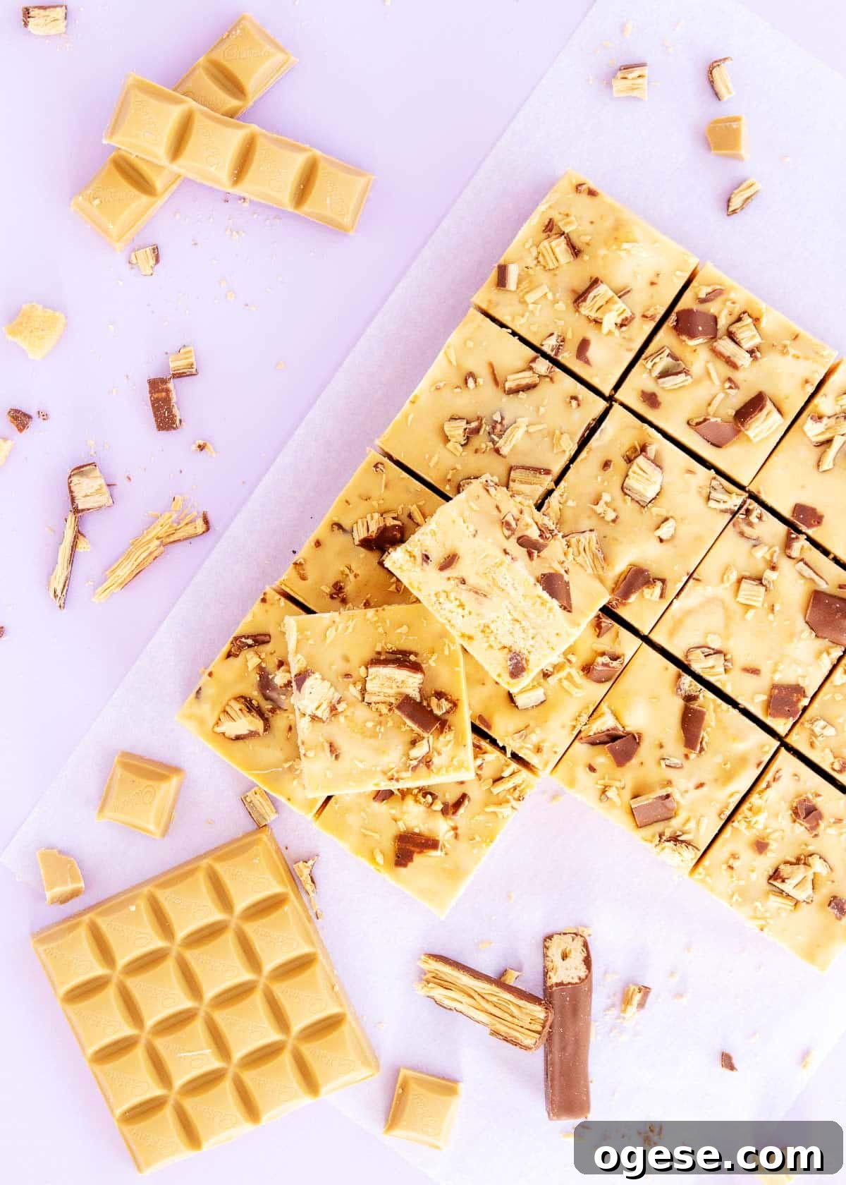 Two squares of slice, sitting on the remaining 14 squares, surrounded by pieces of chocolate and Twirls.