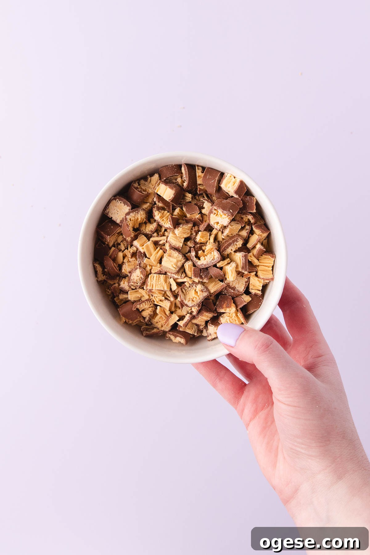 A hand holding a small white bowl of chopped Caramilk Twirls.
