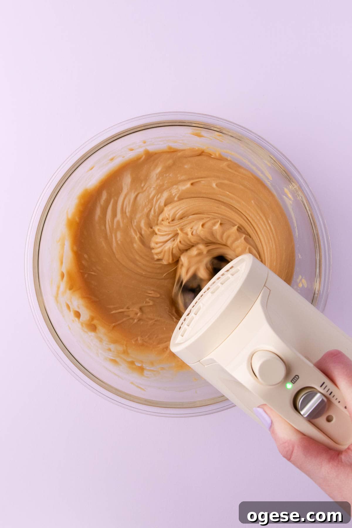 The melted caramilk mixture being beaten with a handheld electric mixer.