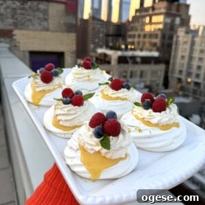 Ale’s Top Easter Recipes 2026: Festive Ideas for Your Holiday 7 A person holds a rectangular platter of mini pavlovas topped with whipped cream, lemon curd, raspberries, blueberries, and mint on a rooftop, with a city skyline in the background at sunset.