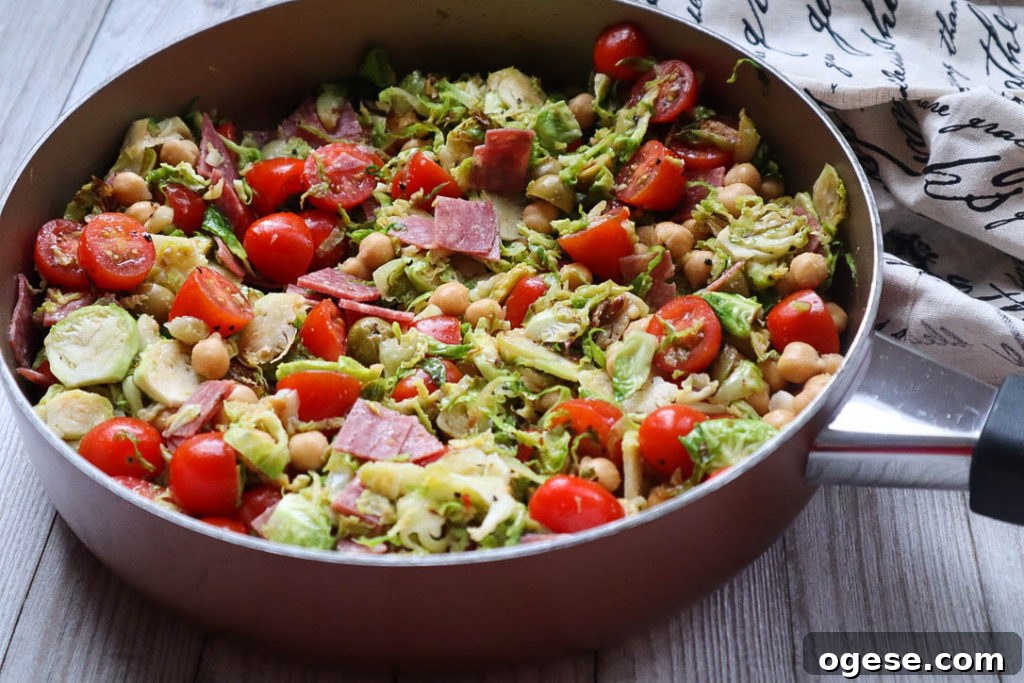 skillet with sauteed brussels sprouts with beans, deli meat, tomatoes, and olives.