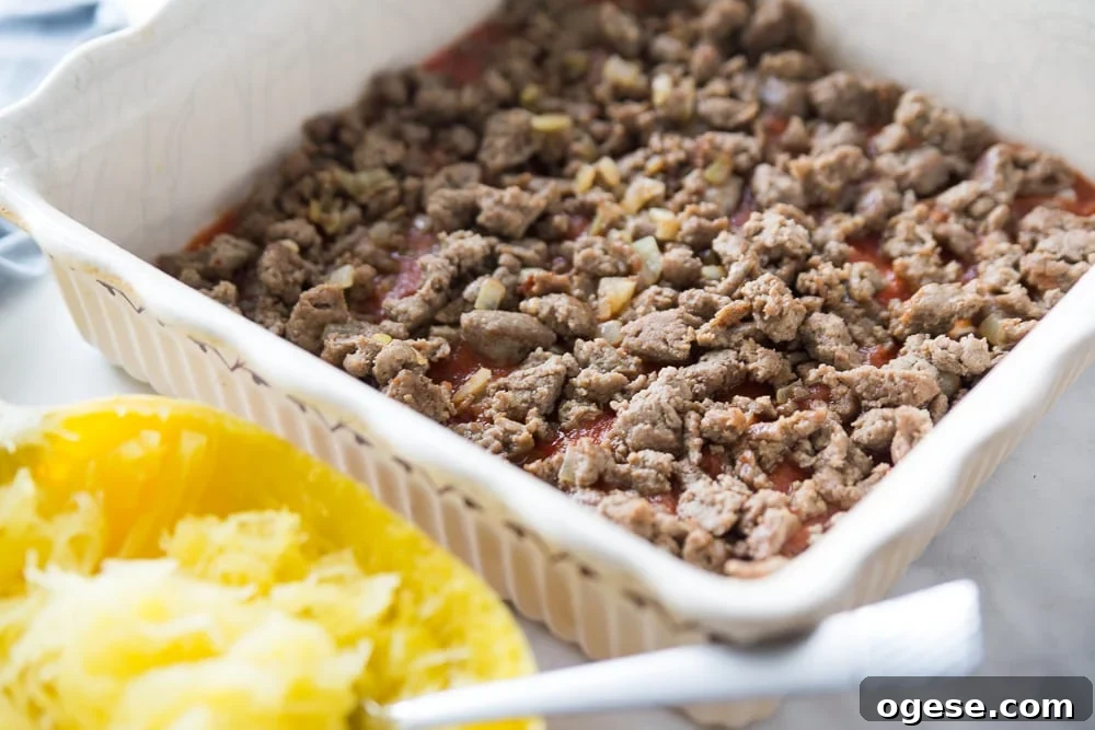 How to Prepare Spaghetti Squash: Simple Steps + Tasty Recipes 4 Half of a cooked spaghetti squash sitting next to a square white baking dish with cooked ground meat and tomatoes