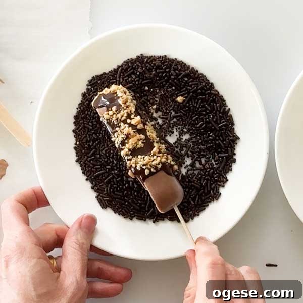Chocolate Peanut Butter Cottage Cheese Ice Cream Bars — High-Protein Treat 14 Rolling the chocolate ice cream bar with melted chocolate and chocolate sprinkles on a white plate.