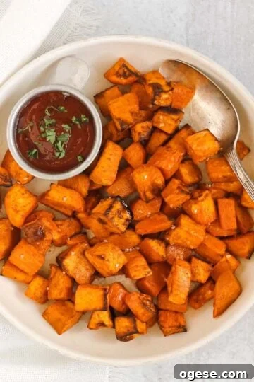 Air fried sweet potato cubes with a vintage serving spoon and side of ketchup on a round cream plate.
