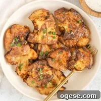 Fried smashed potatoes on a round serving plate with a gold fork.