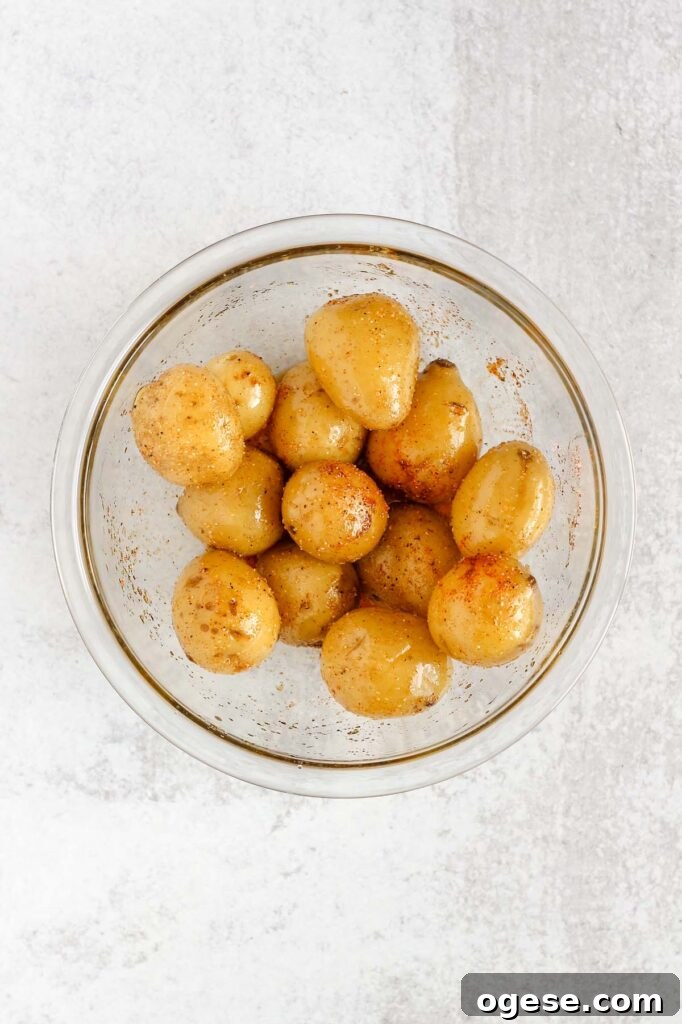 Potatoes tossed in olive oil and seasoning in a mixing bowl.
