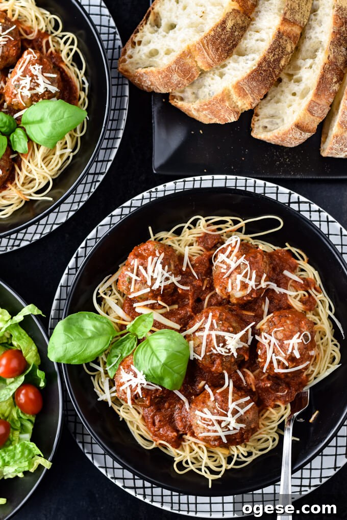 Authentic Homemade Pasta Sauce Recipe for Rich, Simple Flavor 2 Homemade spaghetti and meatballs in a black bowl sitting on a black and white checkered plate. Meatballs are sprinkled with parmesan cheese and a basil sprig garnishes the dish. A green salad, another spaghetti and meatball bowl and crusty bread sits around the main bowl.