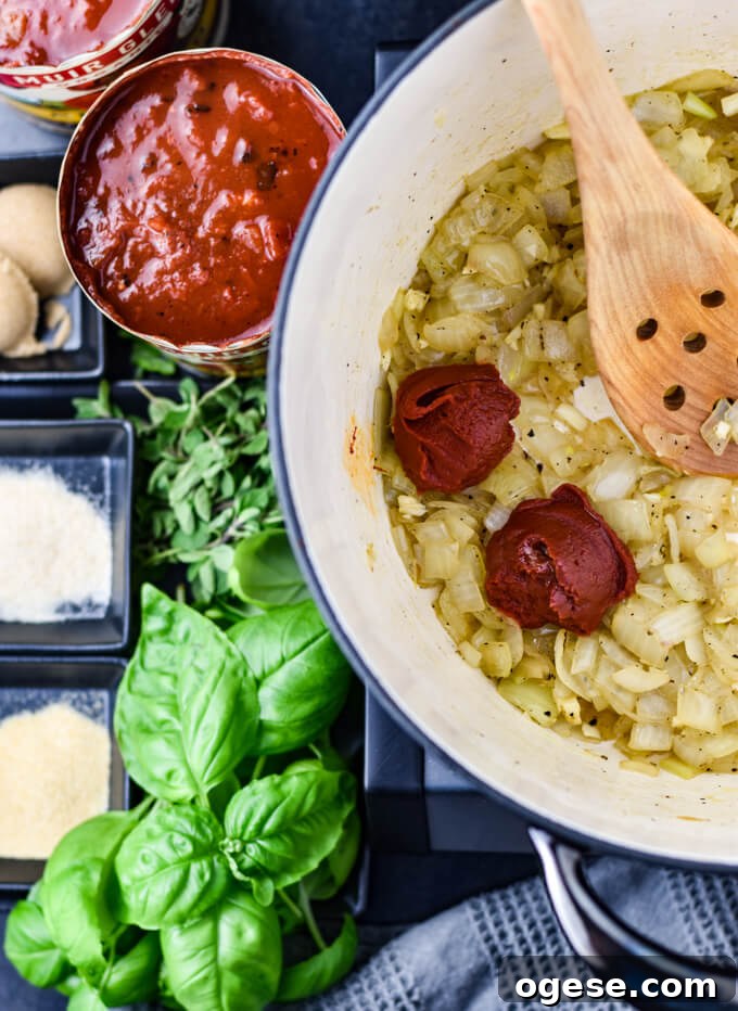 Authentic Homemade Pasta Sauce Recipe for Rich, Simple Flavor 4 A Dutch Oven with sauteed onions and garlic. Two dollops of tomato paste sits on the onions with a wooden bowl in the pan. A can of crushed tomatoes, brown sugar, garlic and onion powder, fresh oregano and fresh basil sit next to the pan.