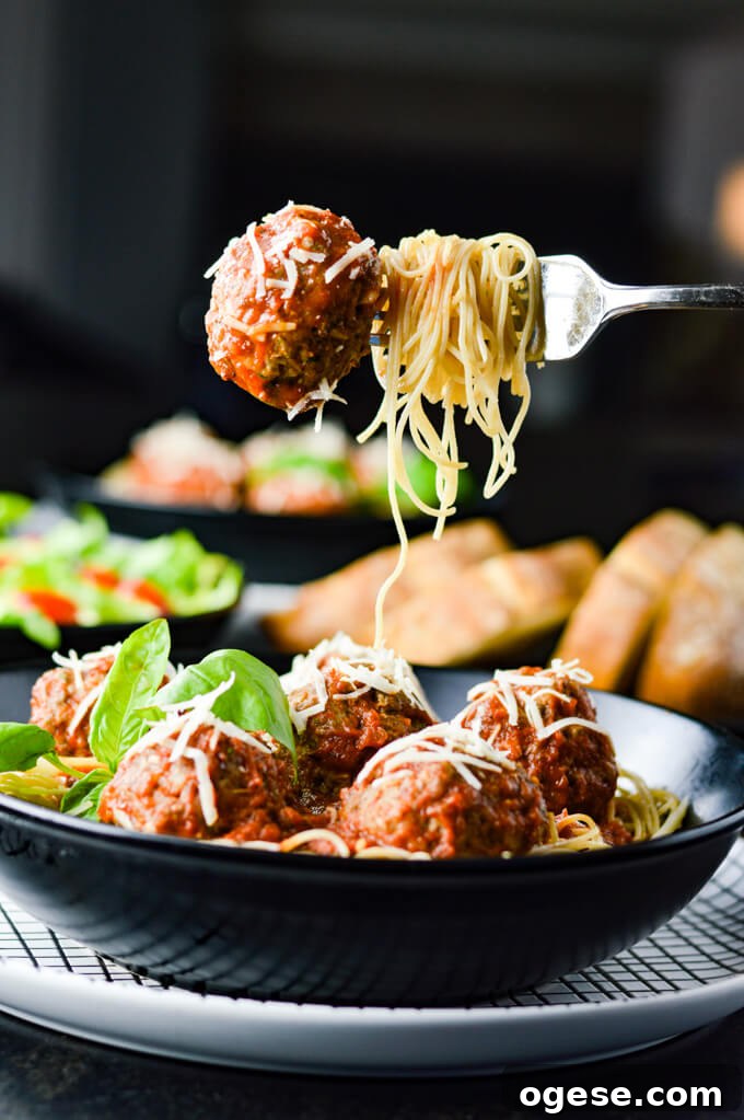 Authentic Homemade Pasta Sauce Recipe for Rich, Simple Flavor 9 A bowl of spaghetti and meatballs. A fork holding swirled spaghetti noodles and a meatball hangs over the plate. A green salad, bread and another bowl of spaghetti sit blurred in the background.