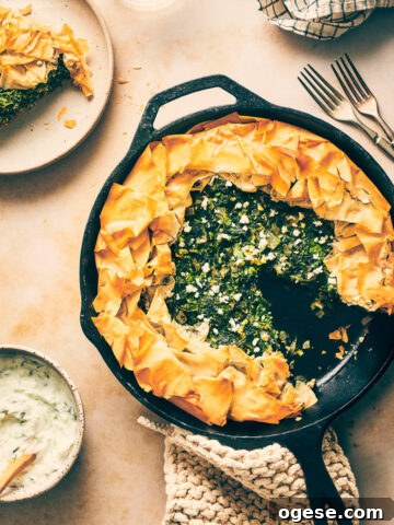 Cast iron pan on the counter with spanakopita slice cut out and served with tzatziki