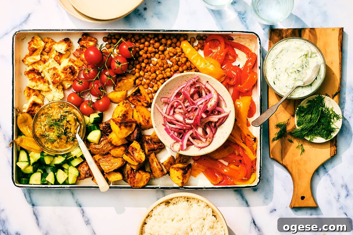 Baked feta, vegetables, roasted chickpeas, and potatoes on a sheet pan with tzatziki.