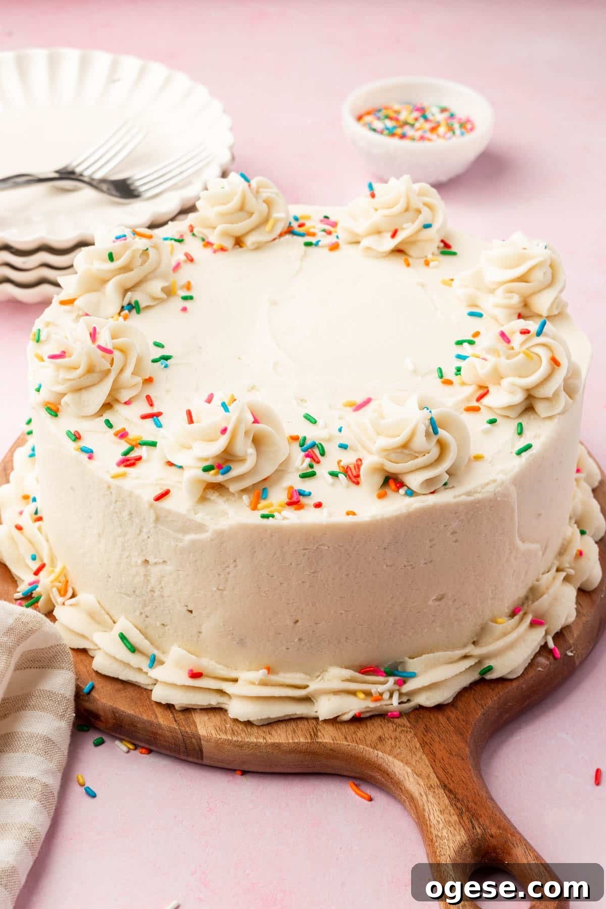 A round gluten free vanilla cake with vanilla frosting and rainbow sprinkles on a wood serving board.