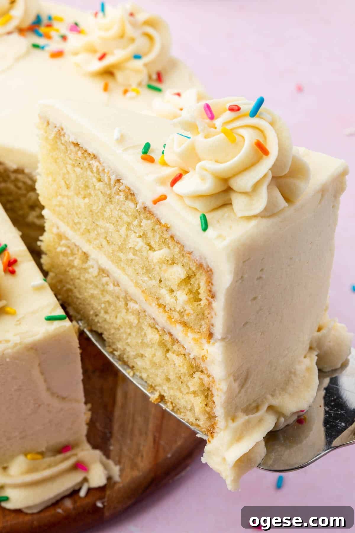 A single slice of 2-layer gluten free vanilla cake topped with rainbow sprinkles being lifted out of the larger cake.