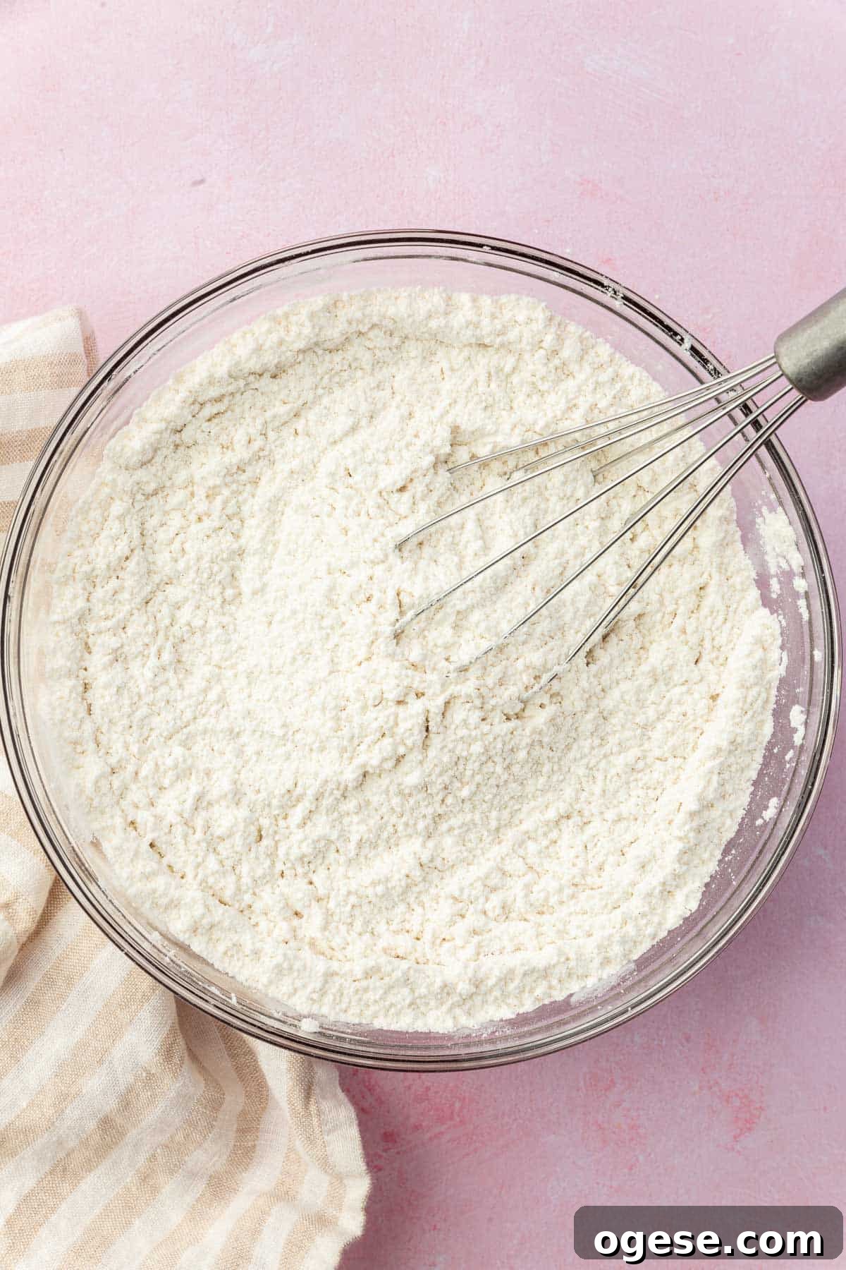 A glass mixing bowl with gluten-free and a whisk in it.