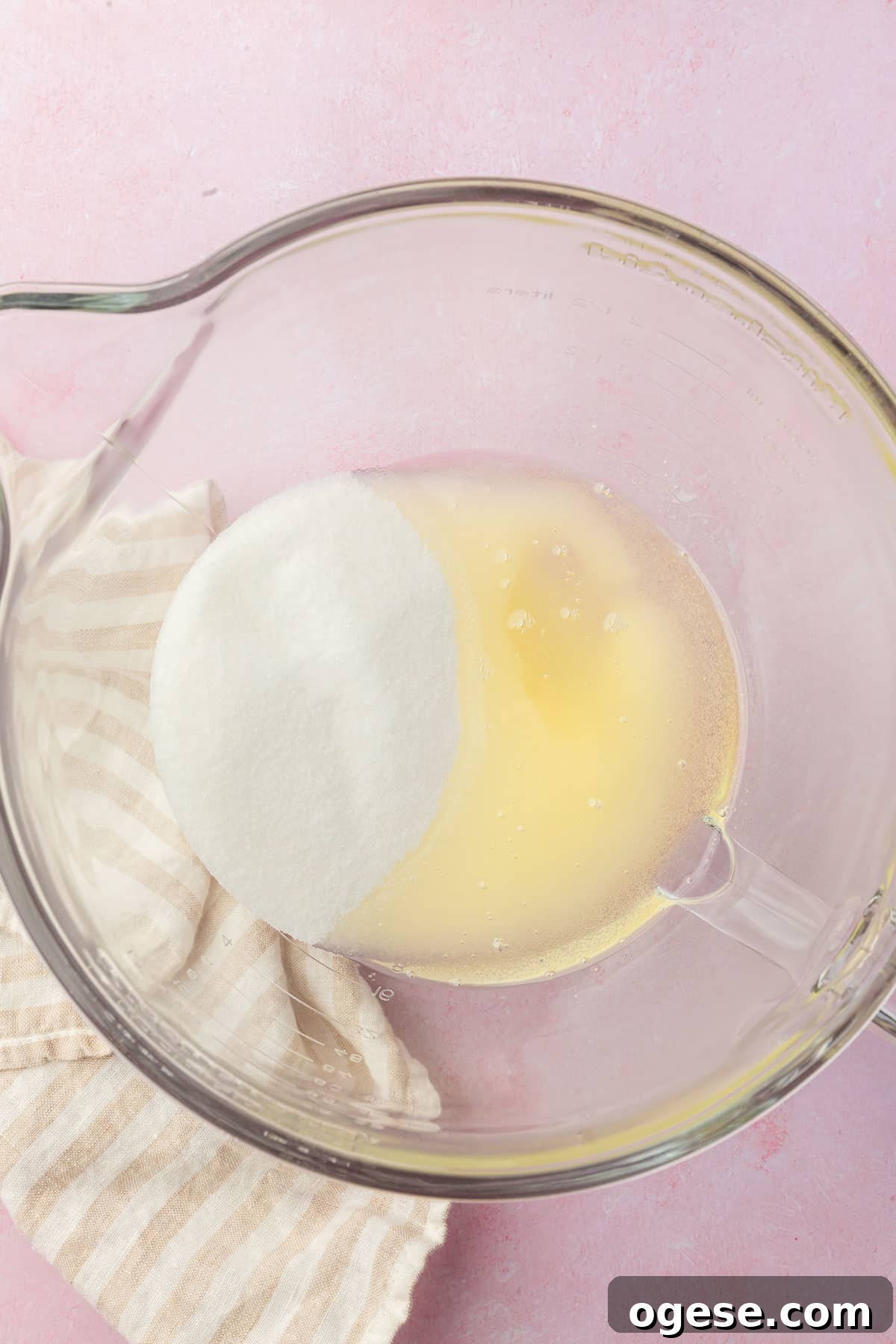 A glass mixing bowl with granulated sugar and oil in it before mixing together.